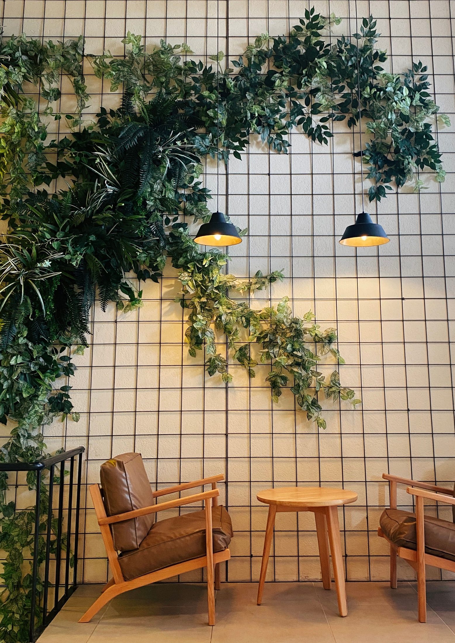 A planted grid wall above two chairs and a small table.